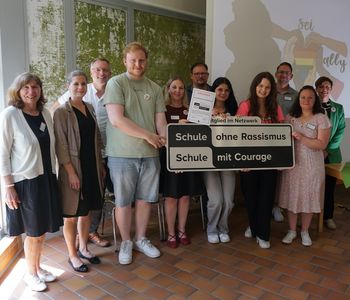 Auszubildende, Lehrkräfte und weitere Personen stehen in Gruppe und lächeln in die Kamera. Sie halten das Schild von Schule ohne Rassimus hoch