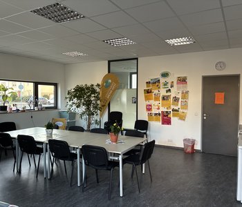 Ein Blick in das Stadtteilbüro Speyer-West: Das Foto zeigt einen großen Tisch mit Stühlen und eine Beachflag mit der Aufschrift "Stadtteilbüro"