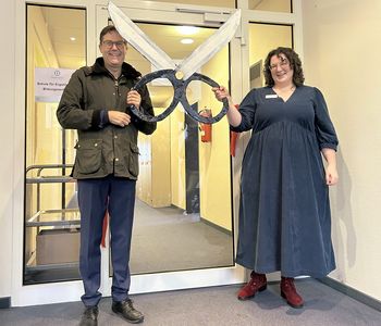 Paul Bomke, Geschäftsführer, und Alessa Boebel, fachliche Leiterin, mit einer symbolischen übergroßen Schere aus Pappe, nachdem sie ein rotes Band an der Tür durchtrennt und damit die Schule offiziell eröffnet haben.