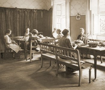 Das Bild zeigt Frauen, die an Tischen sitzen und Körbe flechten.