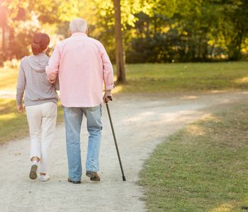 Symbolbild: Frau spaziert mit älterem Mann am Stock