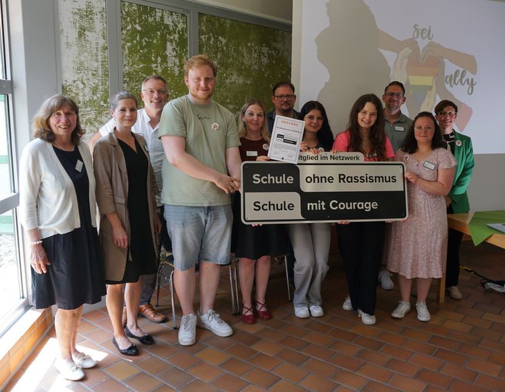 Auszubildende, Lehrkräfte und weitere Personen stehen in Gruppe und lächeln in die Kamera. Sie halten das Schild von Schule ohne Rassimus hoch